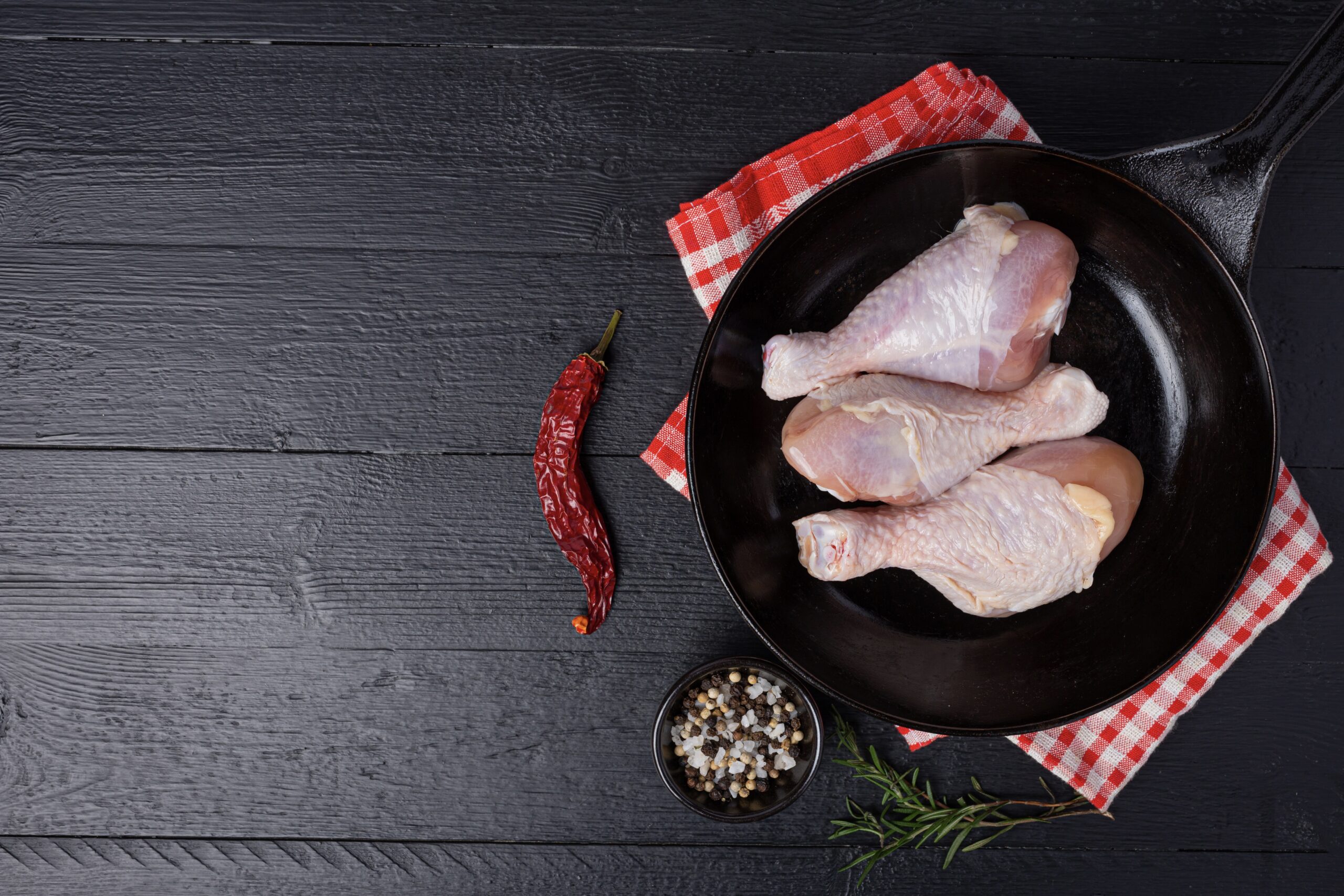 Raw uncooked chicken legs on the dark wooden background.